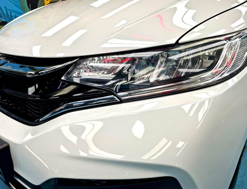 Close-up of the headlamp with light reflections on the white bonnet edge.