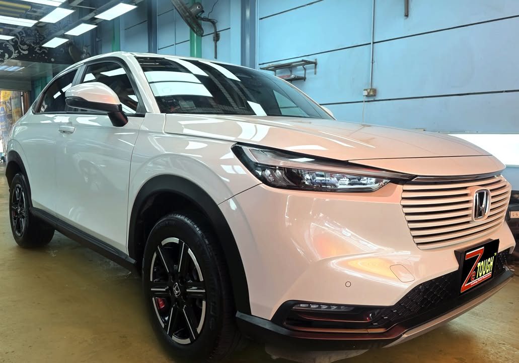 White Honda Vezel, front three-quarter view in the workshop, with a ZeTough plate on the front bumper.