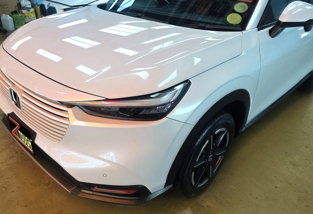 Front corner of the white Vezel showing the bonnet, slatted grille and front wheel.