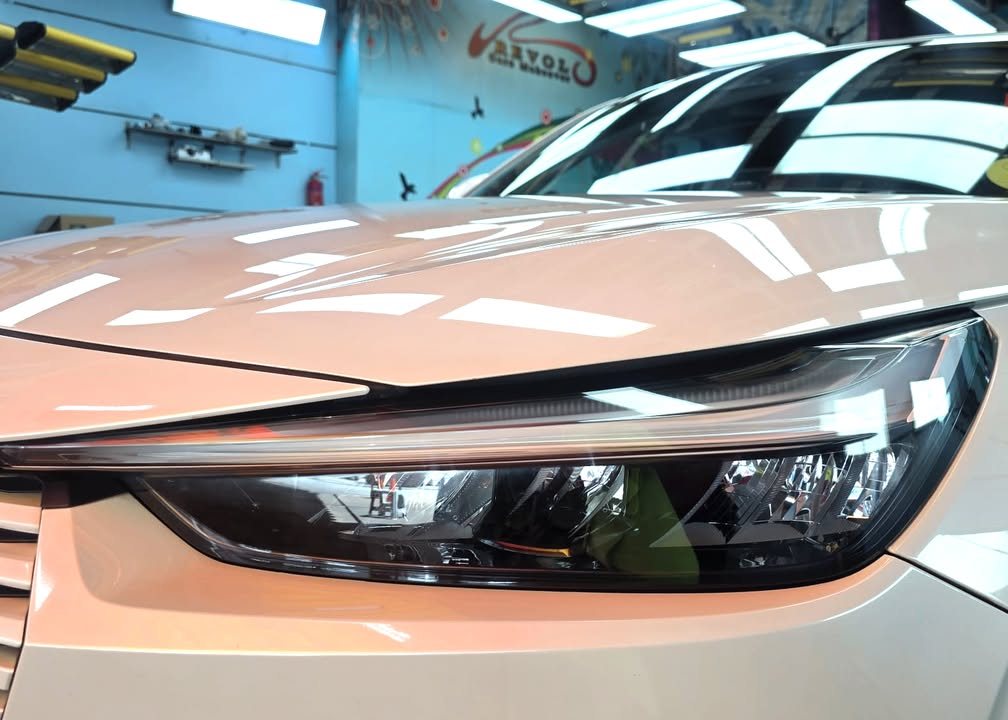 Close-up of the LED headlight and glossy white bonnet edge reflecting the workshop lights.