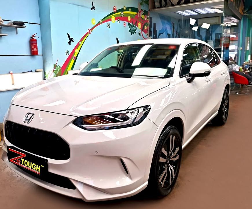 White Honda ZR-V, front three-quarter view in the workshop with a ZeTough plate on the bumper.