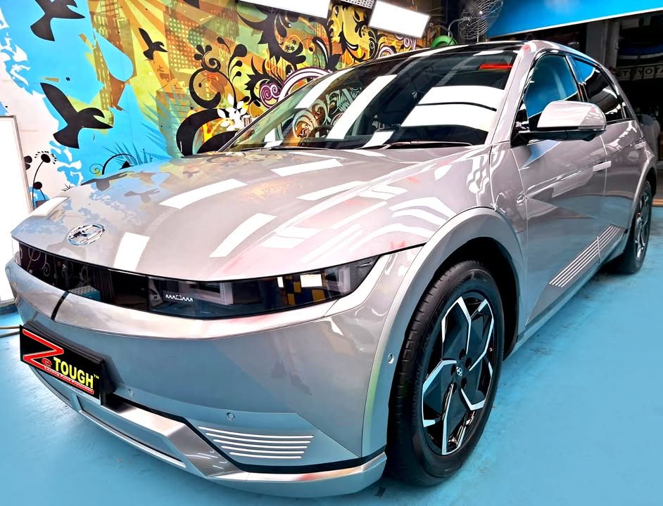 Silver grey Hyundai Ioniq 5, front three-quarter view in the workshop, with ceiling lights reflected in the bonnet and a ZeTough plate on the front.