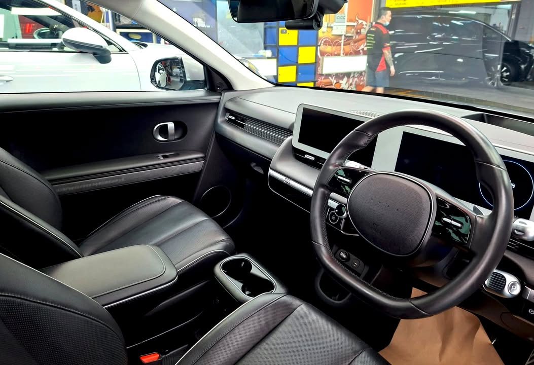 Cabin with dark leather seats, steering wheel and dashboard screens.
