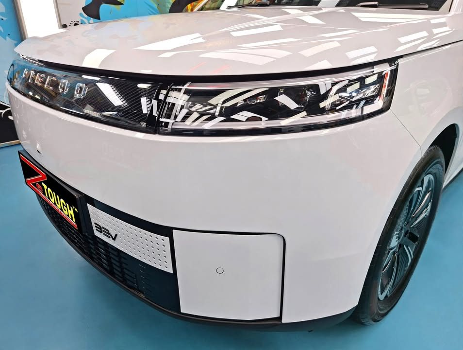 Front of the white Jaecoo J5 showing the full-width headlight strip and bonnet shine.