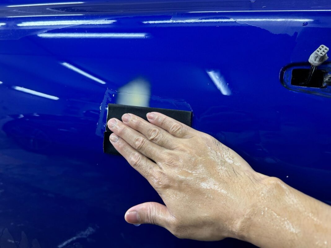 Wet-sanding the Jaguar XF's surface after putty work to level the panels.