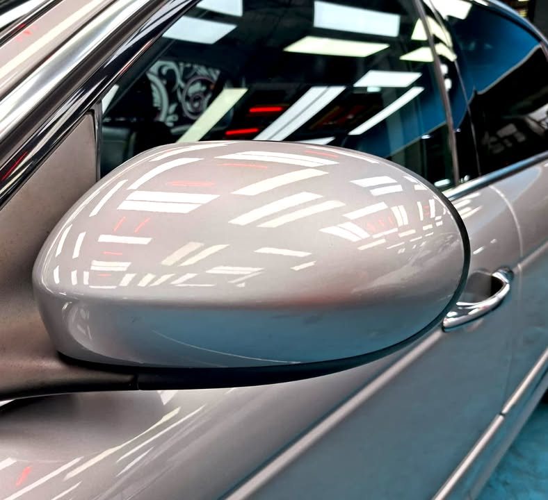 Silver wing mirror on the Jaguar XJ8 with light reflections.