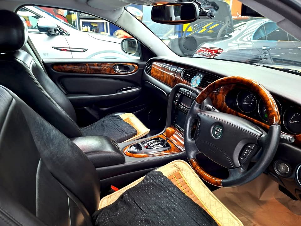 Jaguar XJ8 cabin with wood-rim steering wheel, wood trim and black leather seats.