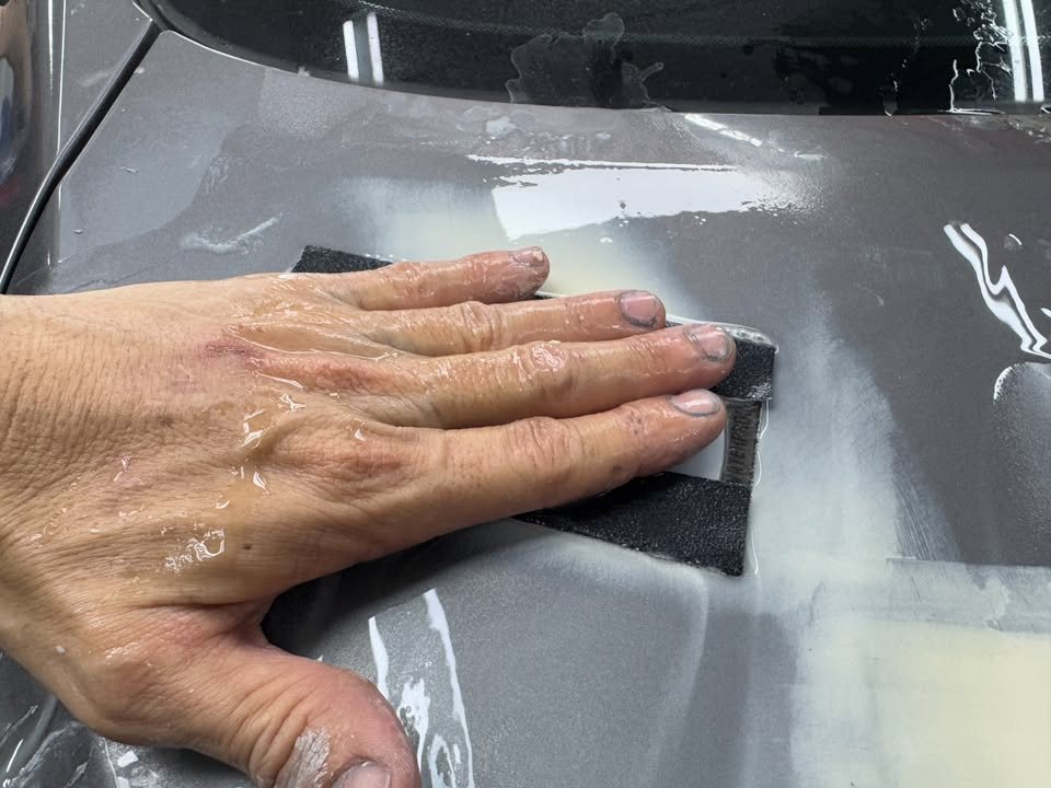 Hand wet-sanding a primed area on the grey panel.