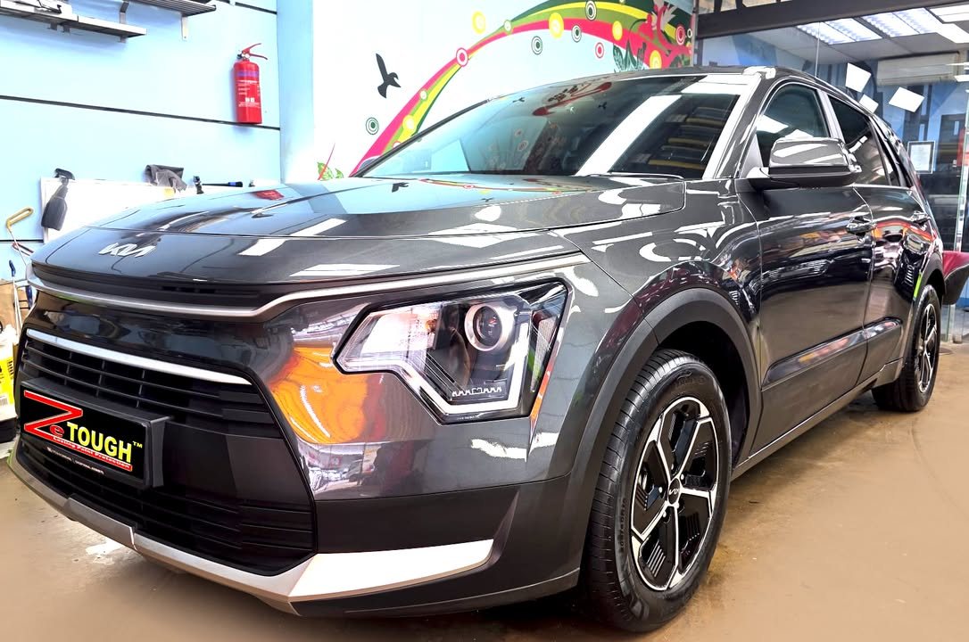 Dark grey Kia Niro, front three-quarter view in the workshop, with a ZeTough plate on the front bumper.