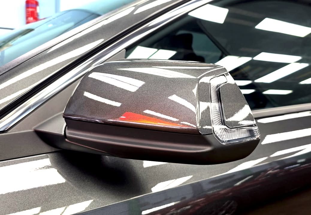 Dark grey side mirror cap reflecting the ceiling lights.
