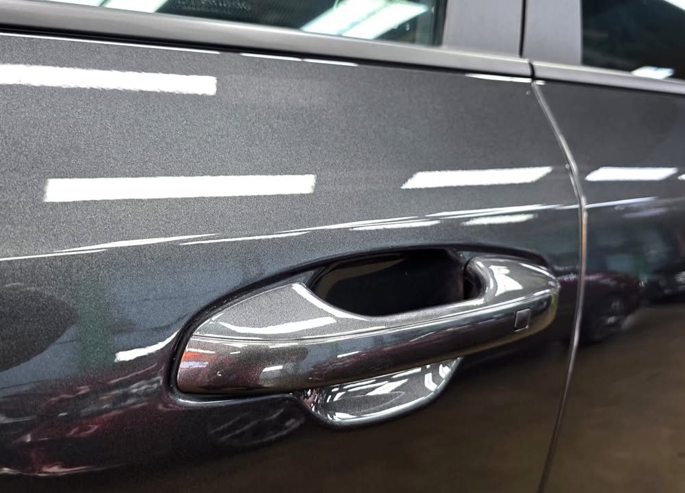 Door handle and door panel with ceiling lights reflected in the metallic paint.