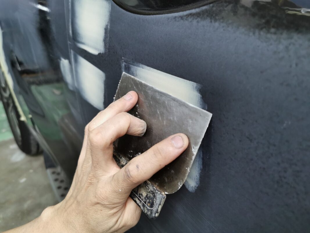 Sanding body filler smooth on a panel of the Kia Sorento before paint.