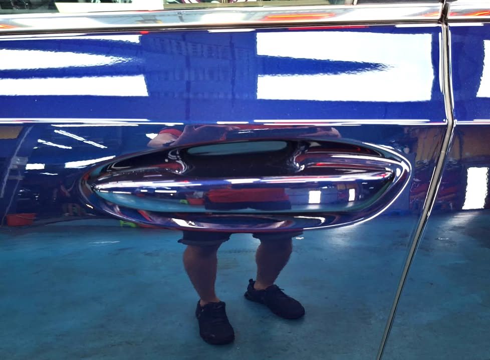 The dark blue door around the handle, with a reflection of a person standing beside it.