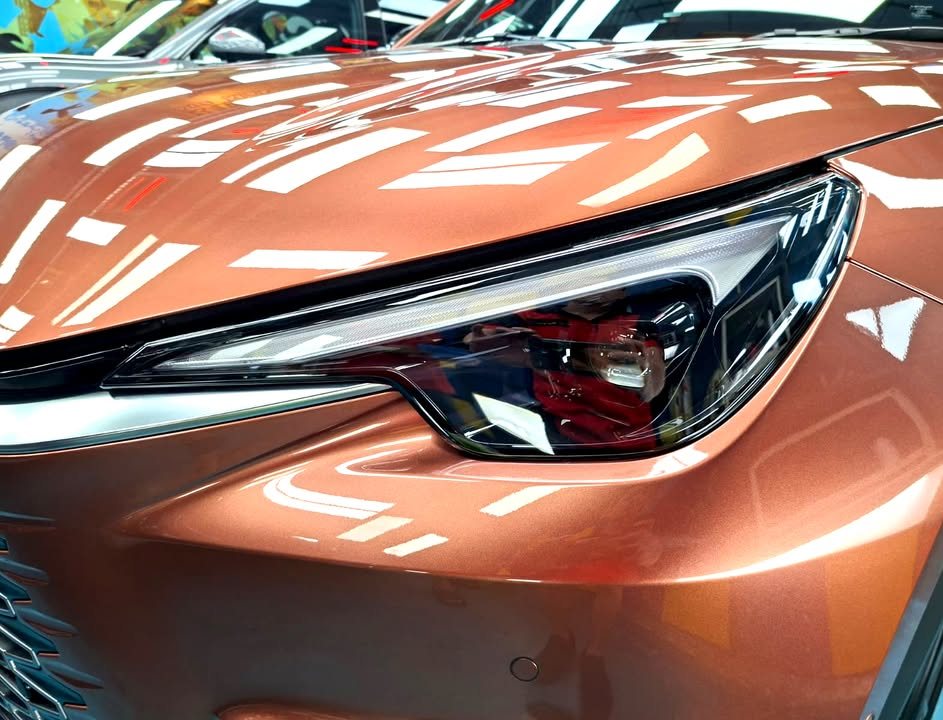Close-up of the Lexus LBX headlamp with workshop lights reflected in the copper paint.