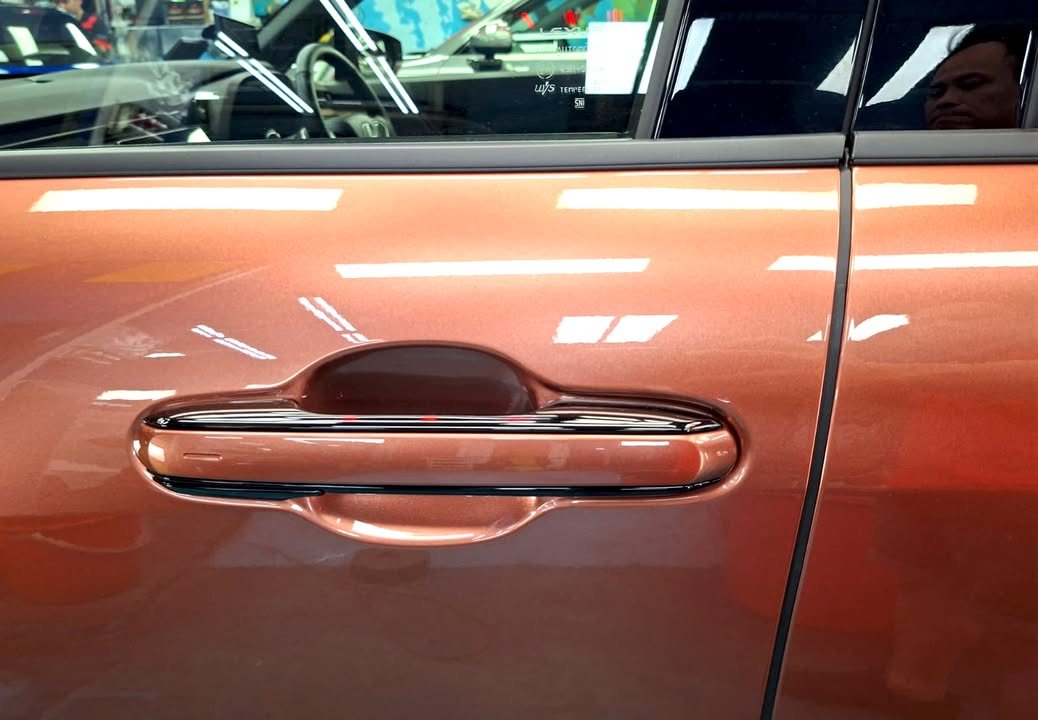 Door handle on the copper Lexus LBX with reflections across the door panel.