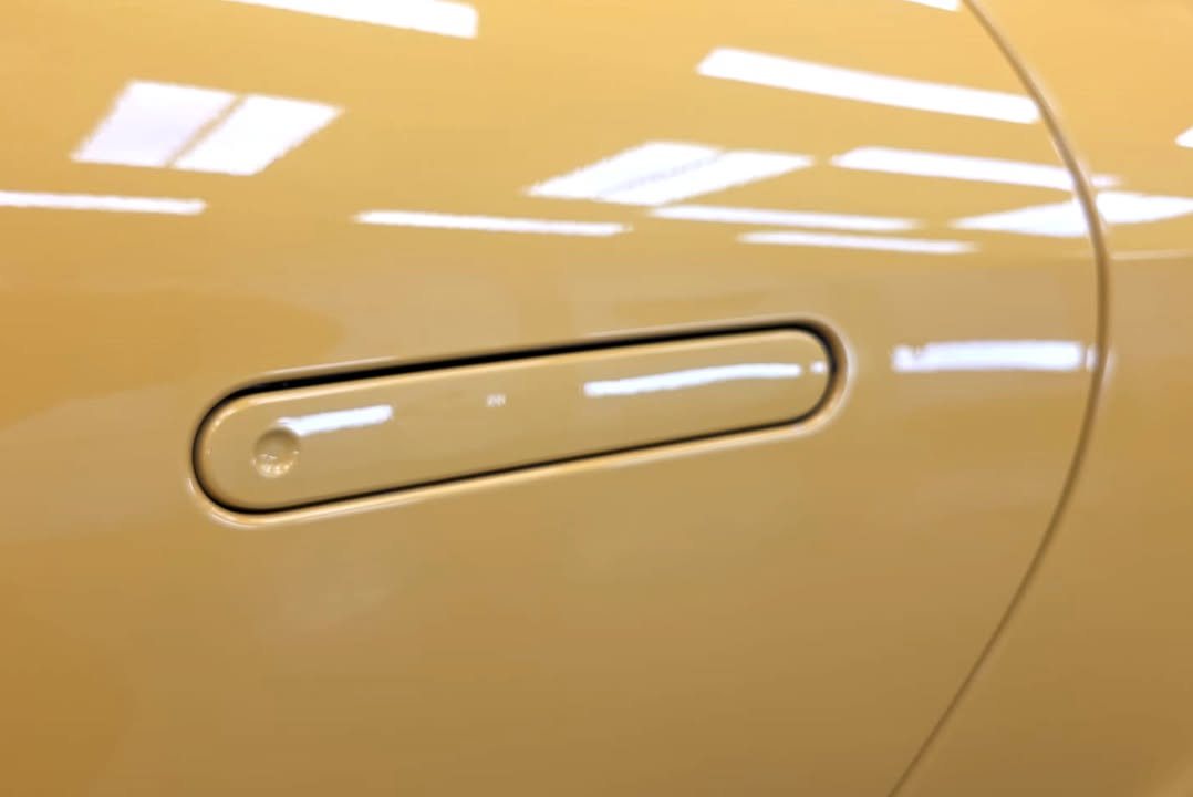 Yellow door panel with flush handle reflecting the workshop lights.