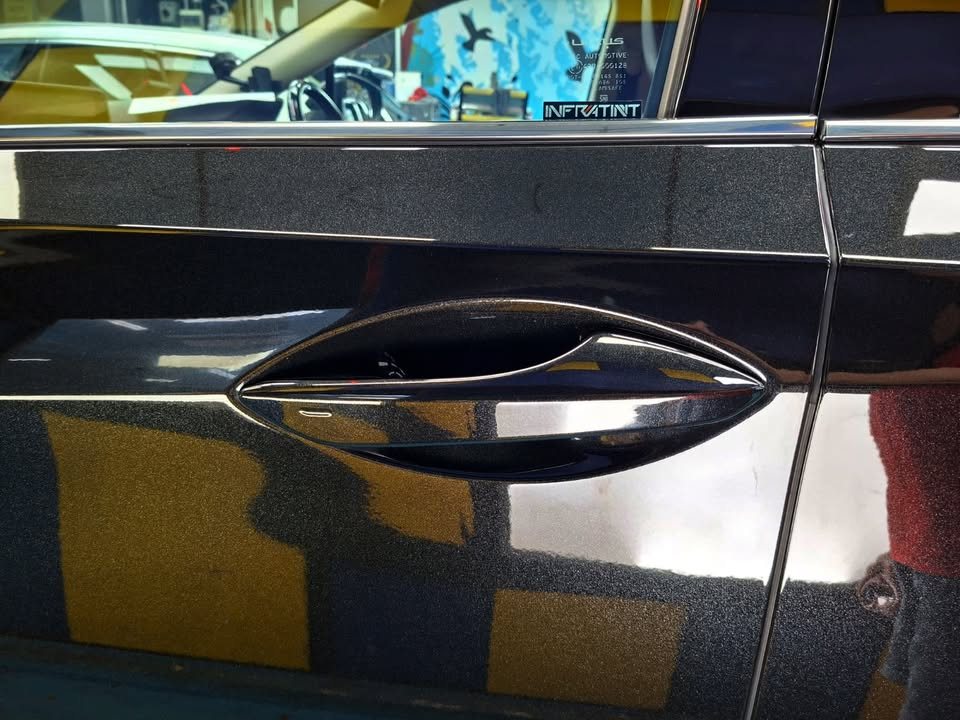 Black door panel and handle reflecting the workshop.