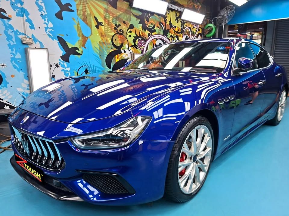 Blue Maserati Ghibli, front three-quarter view, with workshop lights reflected on the bonnet after its ZeTough Ceramic treatment.