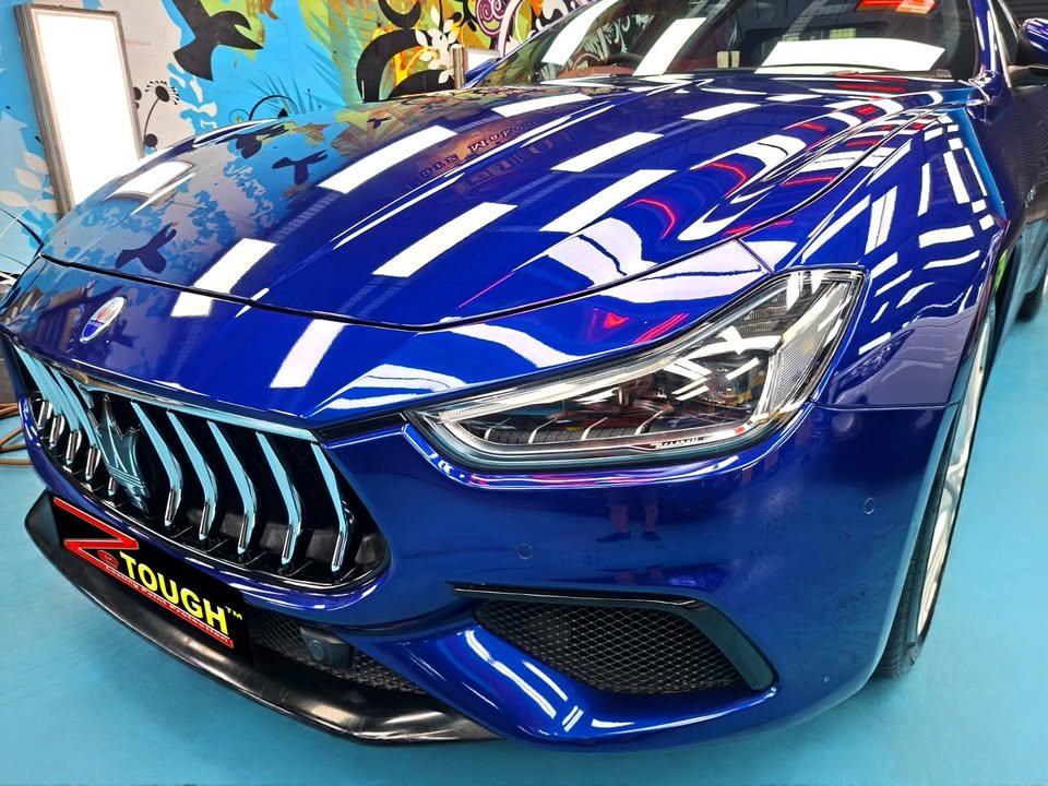 Close-up of the Ghibli grille and blue bonnet reflecting the ceiling lights.