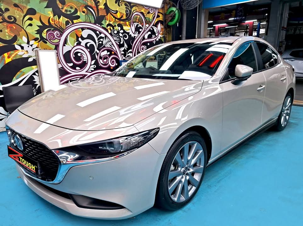Silver Mazda 3 sedan, front three-quarter view, with workshop lights reflected on the bonnet after its ZeTough Ceramic coating.