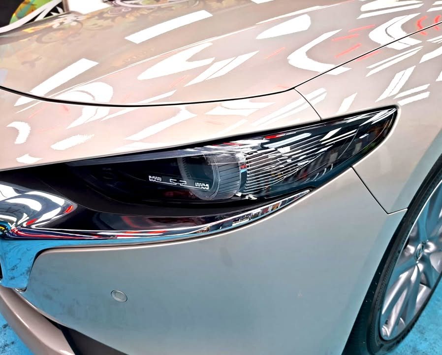 Close-up of the Mazda 3 headlamp beside the silver front wing.