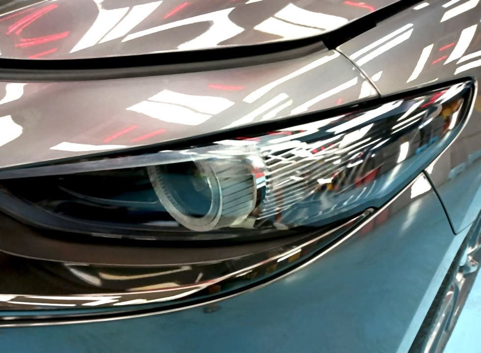 Close-up of the headlight below the glossy grey bonnet edge.