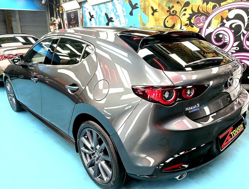 Rear three-quarter view of the grey Mazda 3 hatchback with round red tail lights.