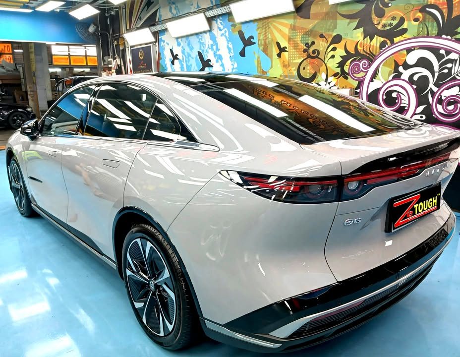 Rear three-quarter view of the light grey Mazda 6e showing the full-width tail light.
