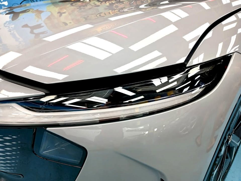 Close-up of the Mazda 6e headlight with studio lights reflected in the bonnet.