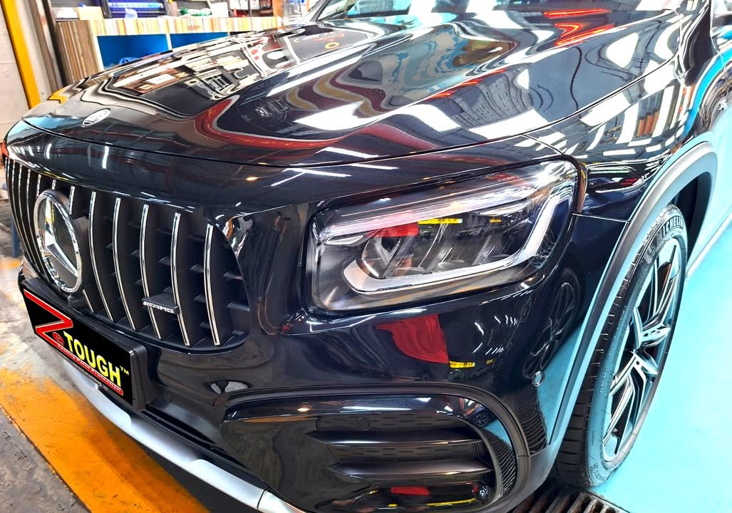 AMG grille and headlight of the black GLB 35 with workshop lights reflected in the paint.