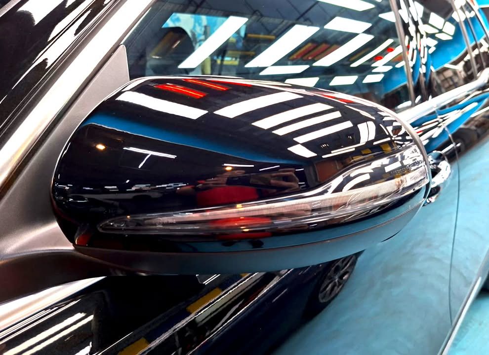 Glossy black wing mirror reflecting the workshop lights.