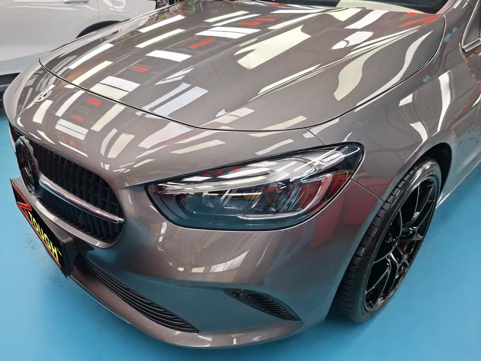 Close-up of the Mercedes-Benz B 180 grille and headlight with lights reflected in the grey bonnet.