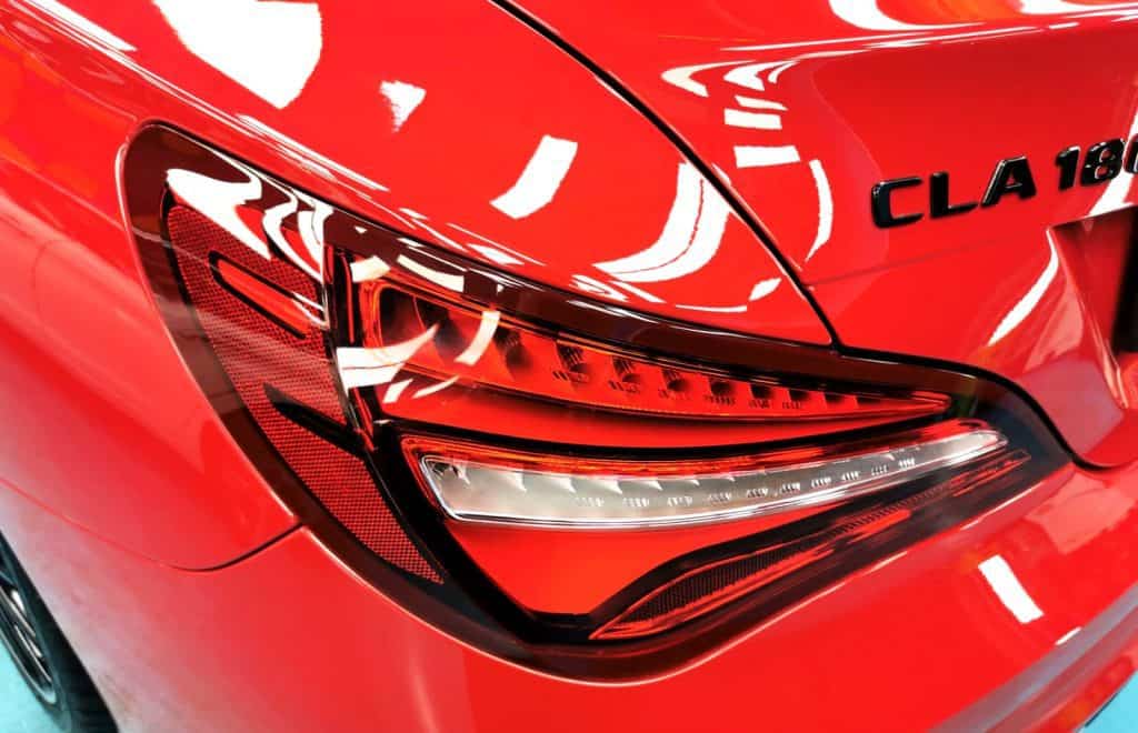 The coated bonnet of the red Mercedes-Benz CLA 180 under workshop lighting.