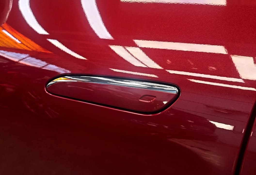 Red door panel and flush handle reflecting the workshop lights.