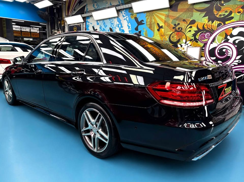 Rear three-quarter view of the black Mercedes-Benz E200 after its respray, glossy paint reflecting the workshop lights.
