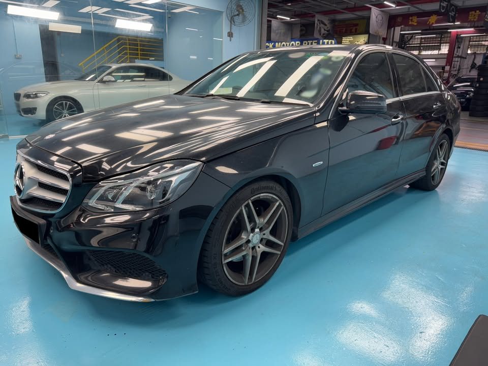 Front three-quarter view of the black Mercedes-Benz E200 parked on the blue workshop floor.