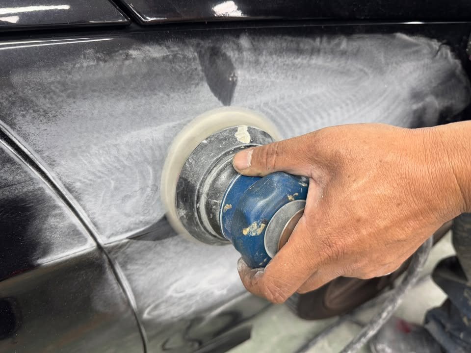 A machine sander working across a wet, sanded black panel.