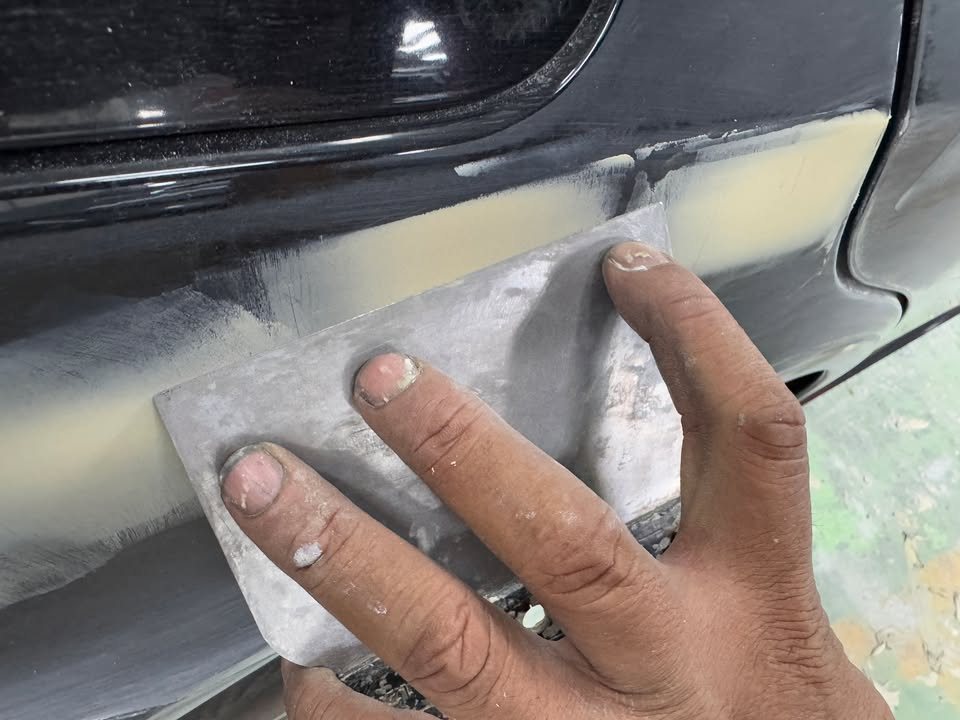 A hand spreading filler over a lower body panel with a metal spreader.