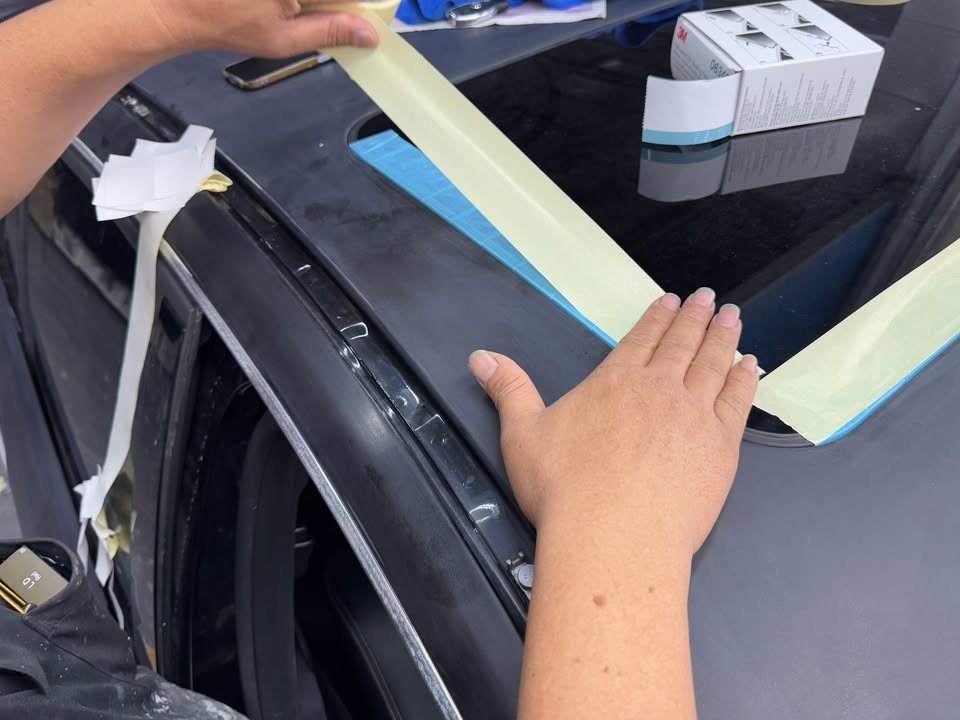 Masking tape being laid along the edge of a black panel.