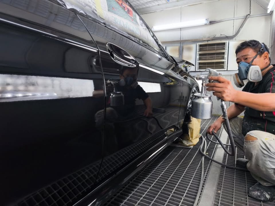 A painter in a respirator spraying the side of the black E200 inside the spray booth.