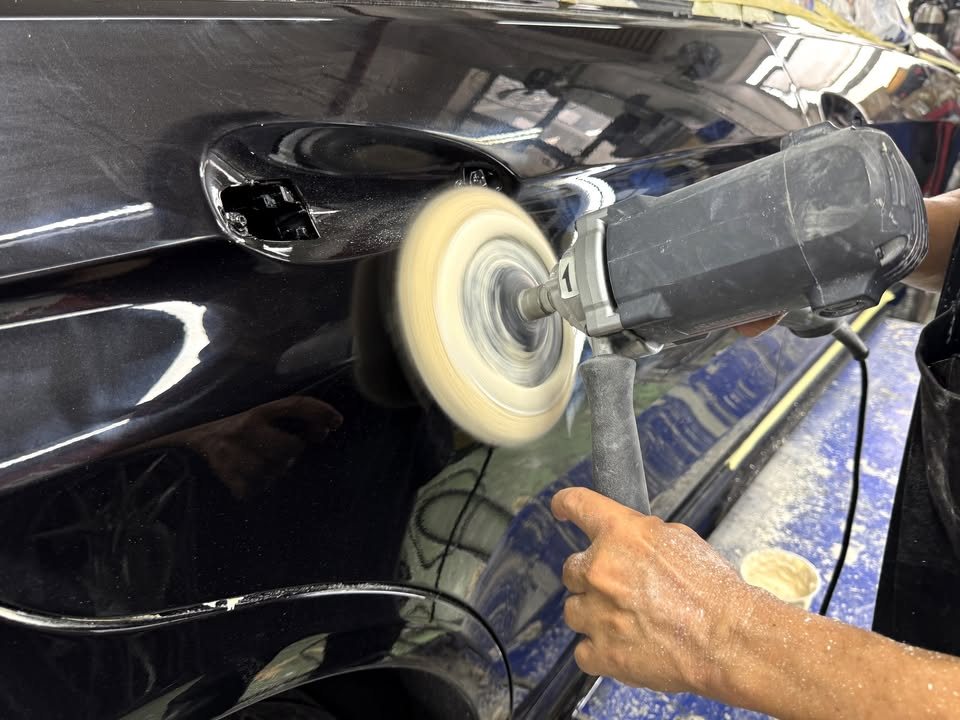 A rotary polisher with a foam pad polishing the black front bumper.