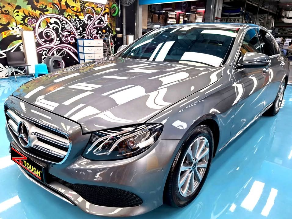 Grey Mercedes-Benz E200 from the front three-quarter, its bonnet reflecting the workshop lights after the ZeTough Ceramic coating.