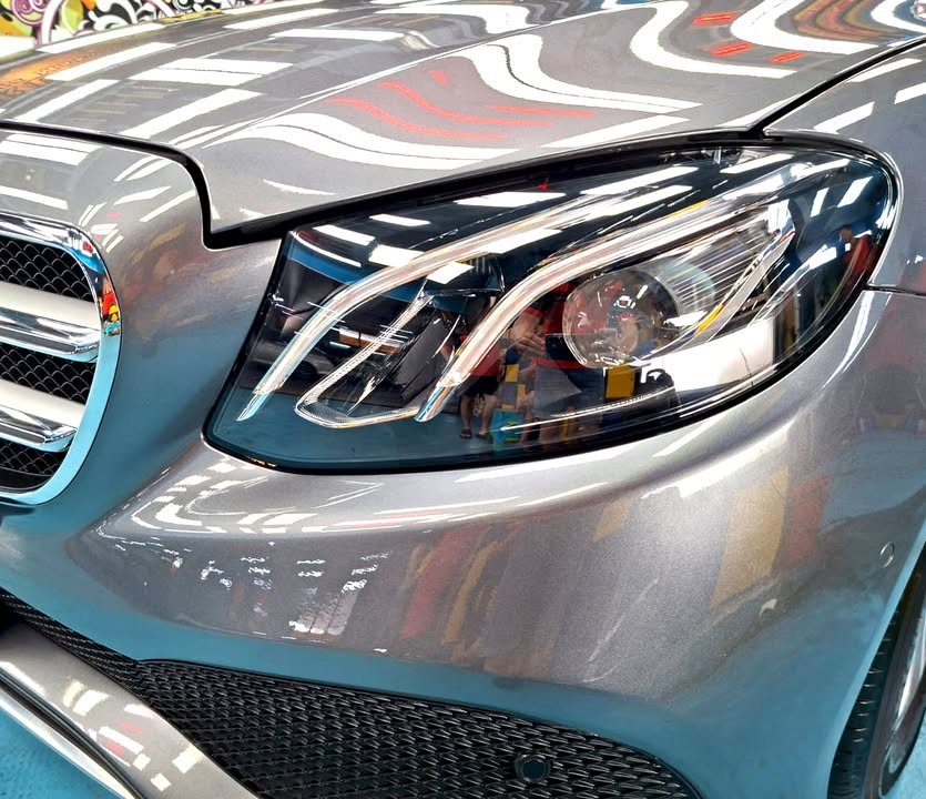 Close-up of the E200's headlamp and front wing with light reflections across the grey paint.