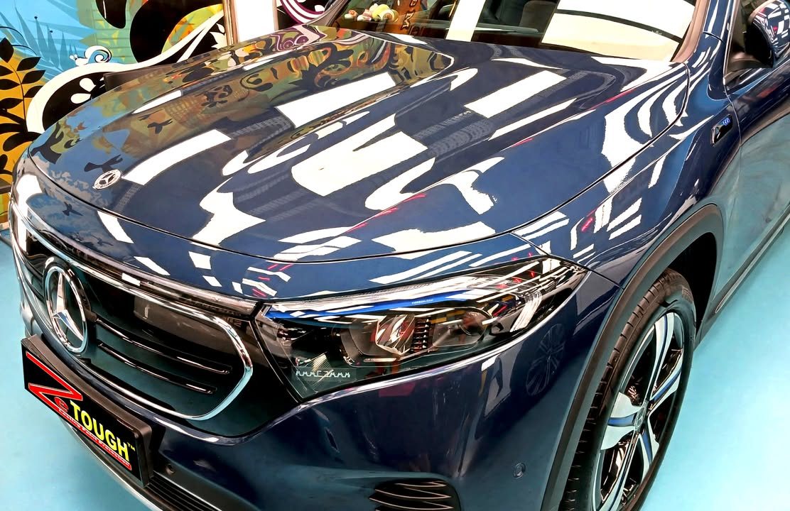 Blue bonnet and front grille of the Mercedes-Benz EQB with workshop lights reflected in the paint.