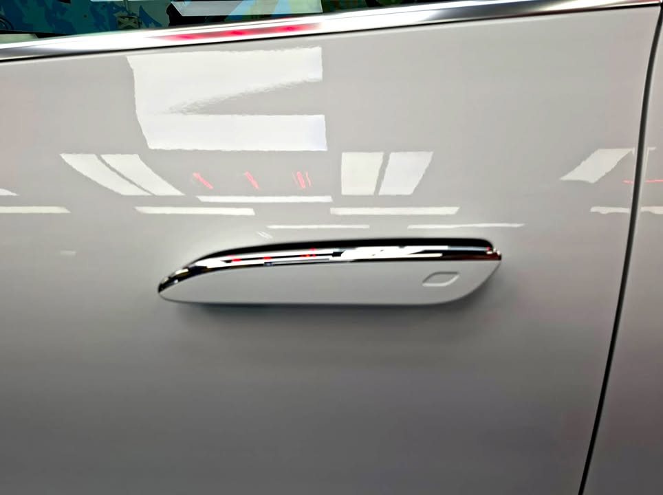 Chrome door handle on the white door panel with workshop lights reflected.
