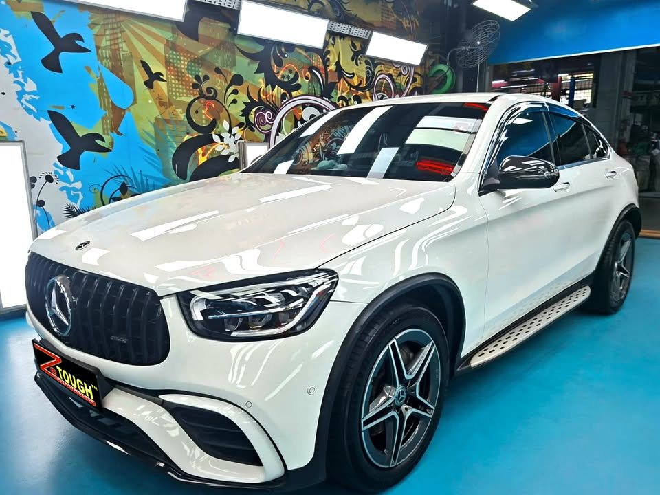 White Mercedes-Benz GLC 300 Coupe, front three-quarter view in the workshop, with a ZeTough plate on the front bumper.