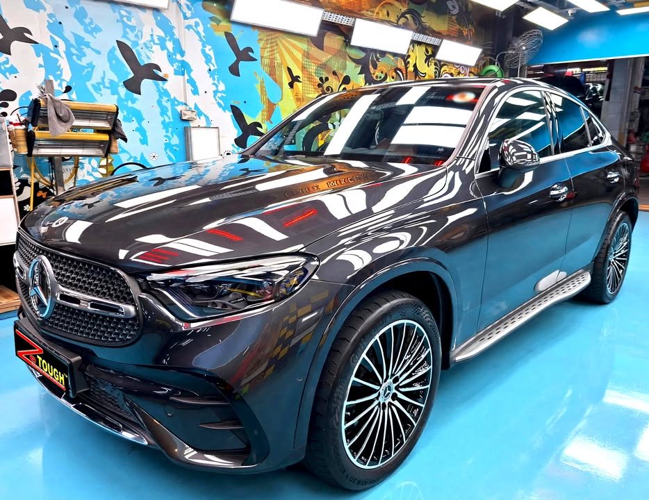 Dark grey Mercedes-Benz GLC 300e Coupe, front three-quarter view in the workshop, with ceiling lights reflected in the bonnet.
