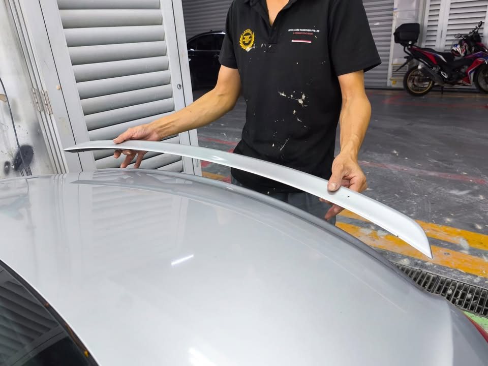 Technician lifting the rear spoiler off the boot lid.
