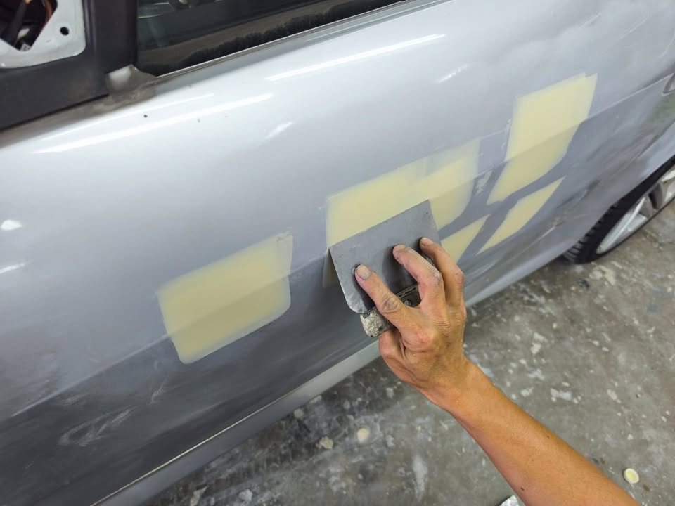Filler patches being smoothed on the door with a spreader.