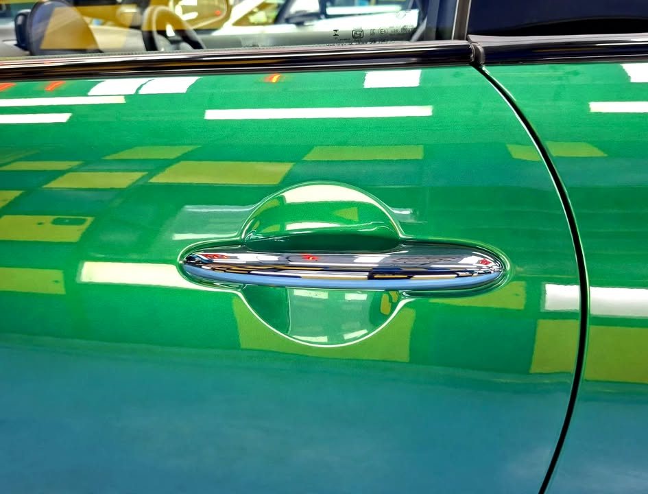 Door handle on the green MINI Cooper with workshop lights reflected in the door panel.